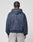 Seen from behind, a person with braided hair wears the LIVE FAST DIE YOUNG Live Fast Berlin Hooded Zip in blue Baumwolle with a graphic and “LIVE FAST BERLIN” on the back, paired with light-wash jeans against a light background.