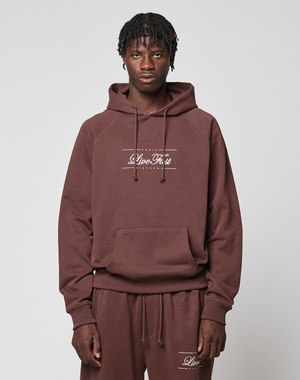 A person wearing a matching brown LFDY Embroidery Hooded and sweatpants by LIVE FAST DIE YOUNG, made from 100% Baumwolle french terry with "Live Fast" in white on both, stands against a light gray background, looking at the camera. | model
