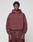A person in an oversized maroon LIVE FAST DIE YOUNG Basic 360 Hooded sweatshirt and matching sweatpants stands facing forward against a plain light gray background. The hoodie features "LifeBag" text on the left chest.