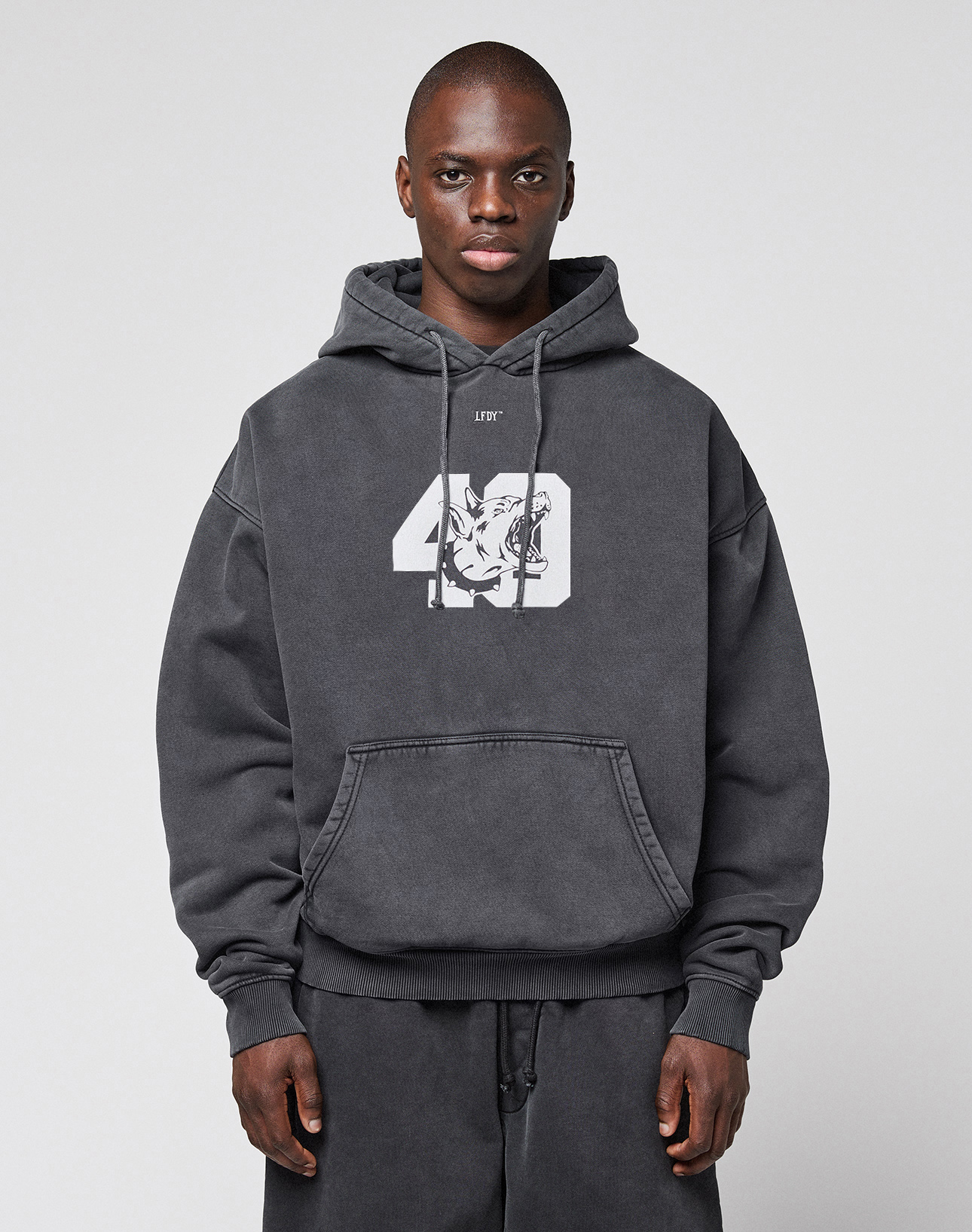 A person wears the LIVE FAST DIE YOUNG LFDY 40 Hooded, an oversize dark gray Baumwolle-Polyester hoodie with a white "49" and graphic on the chest, standing against a light gray background.