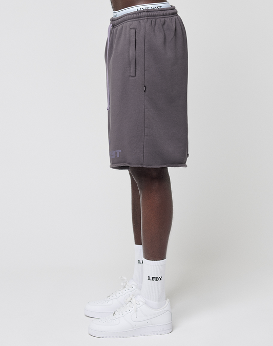 A person stands sideways wearing gray Live Fast LF Shorts by LIVE FAST DIE YOUNG, featuring an elastic waistband and side pockets, paired with white socks and sneakers. Only the lower half is visible against a plain white background.