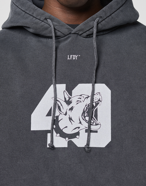 A close-up of a person wearing the LIVE FAST DIE YOUNG LFDY 40 Hoodie in dark gray, featuring white "LFDY" text above a large "40" with a growling dog's head inside the zero and finished with a classic kangaroo pocket for comfort.
