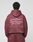 A person in an oversized maroon “Basic 360 Hooded” by LIVE FAST DIE YOUNG, featuring a bold “LiveFast Bordeaux 18-1718” backprint, stands against a plain light background facing away from the camera.