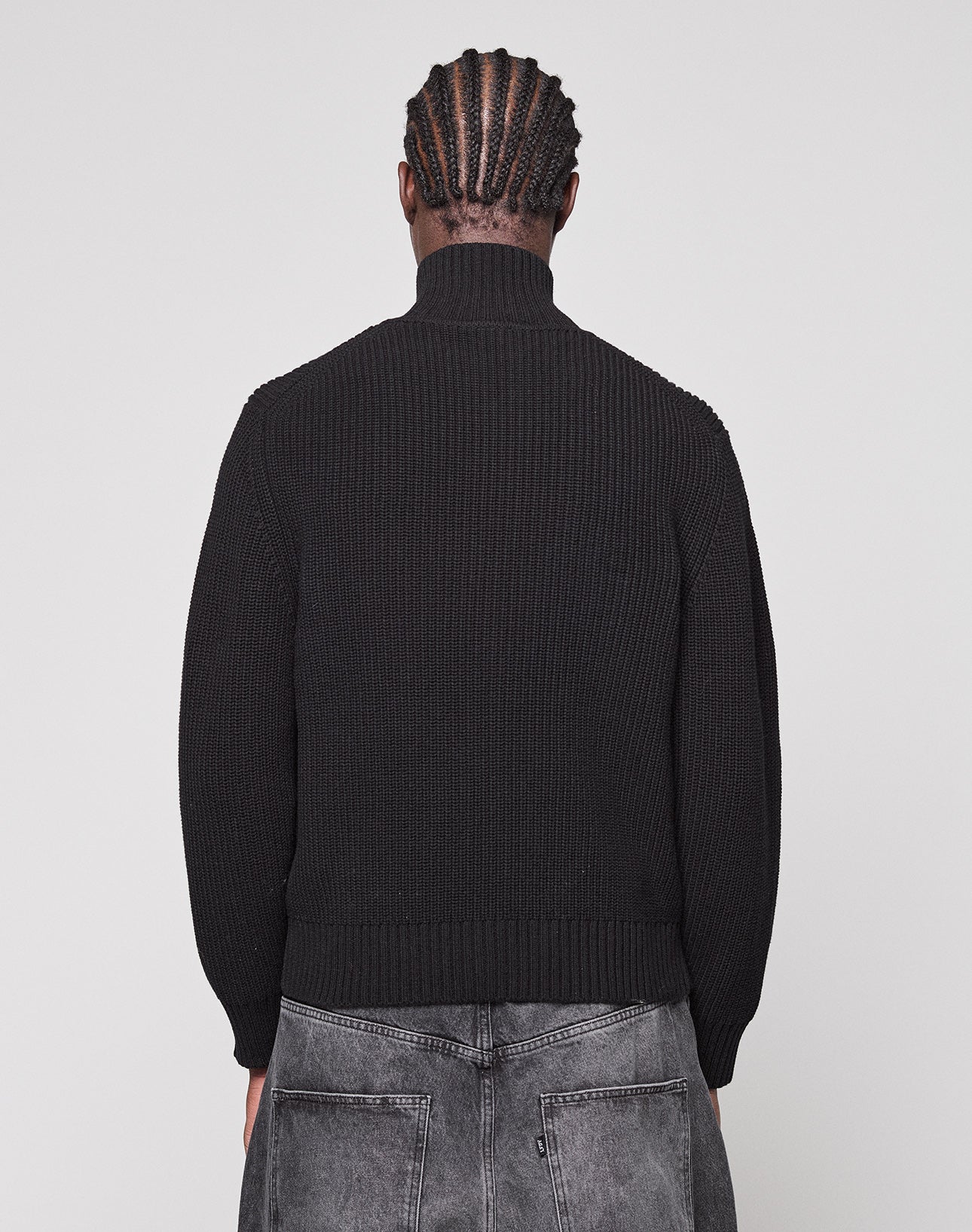 A person with cornrow braids is seen from behind, wearing the LFDY Knit Jacket by LIVE FAST DIE YOUNG and gray washed jeans against a plain light background.