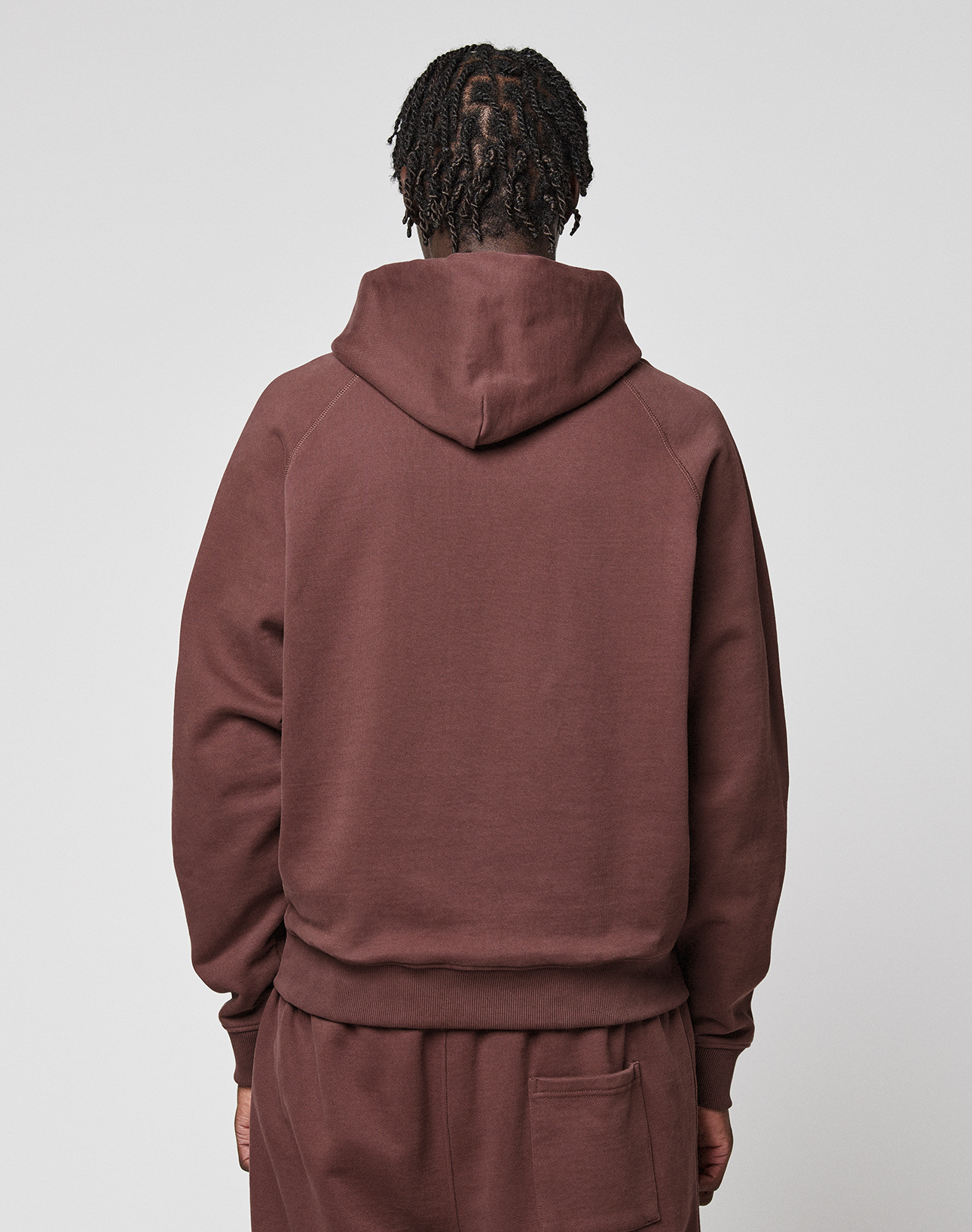 Seen from behind, a person with short, twisted hair wears the LIVE FAST DIE YOUNG LFDY Embroidery Hooded in brown with matching pants, both made from soft French Terry, set against a plain light gray background.