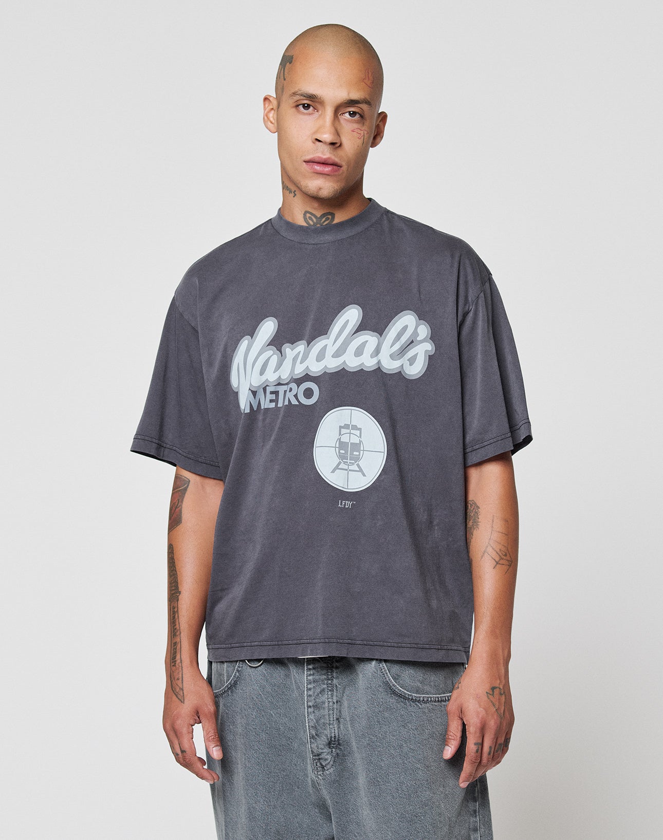A person with a shaved head models the LFDY Vandals Tee by LIVE FAST DIE YOUNG—an oversized, faded gray 100% Baumwolle T-shirt with a bold "Vandals Metro" front print and subway train graphic, against a plain white background.