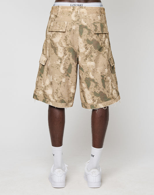 A person faces away wearing LFDY Cargo Shorts by LIVE FAST DIE YOUNG in vintage tie-dye tan and green 100% Baumwolle, a white LIVAST-branded waistband, white crew socks, and white sneakers against a plain light background.