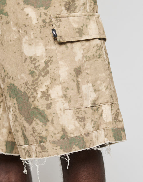 Close-up of the lower body in LIVE FAST DIE YOUNG LFDY Cargo Shorts, made from 100% Baumwolle in beige-green camo. Features a worn hem, large flap pocket, and black tag for a signature vintage style.