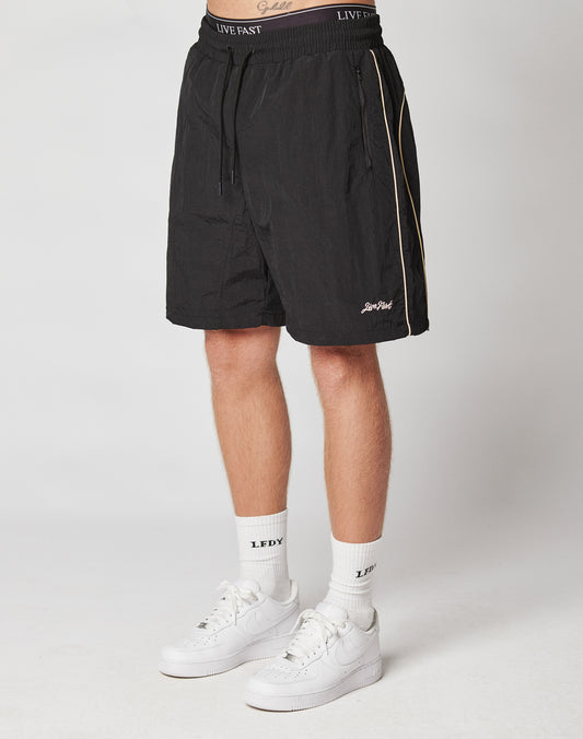 A person wearing LIVE FAST DIE YOUNG Beach Shorts, white crew socks with LFDY text, and white Nike sneakers stands against a plain light background.