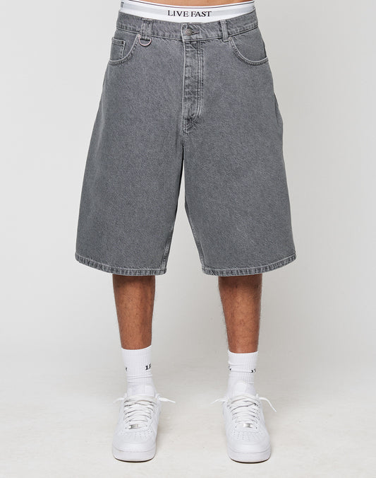 A person wears LFDY Jorts by LIVE FAST DIE YOUNG—loose, knee-length gray denim shorts with a wide straight leg. Styled with white socks, white sneakers, and LIVE FAST waistband underwear. Photo taken against a plain background.