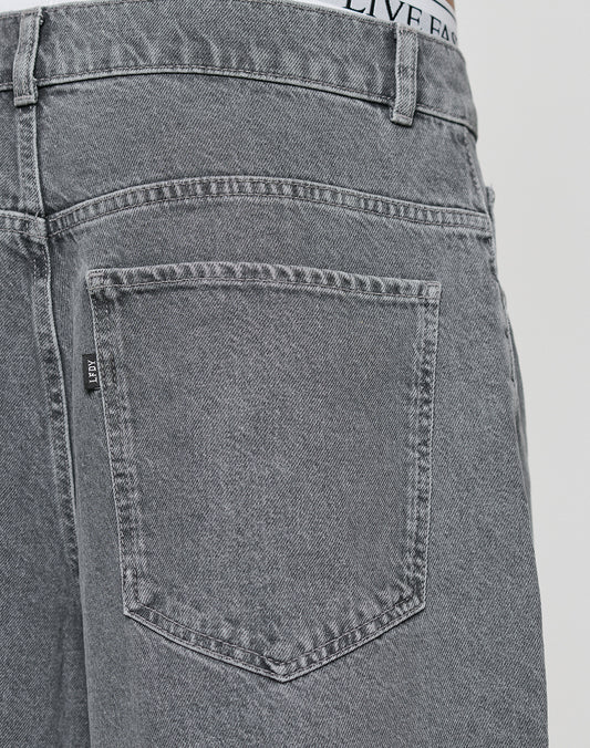 Close-up of the back pocket and waistband of LIVE FAST DIE YOUNG LFDY Jorts in gray denim with a baggy, weites gerades Bein fit. Features detailed stitching and a small woven label on the pocket seam, worn by a model.