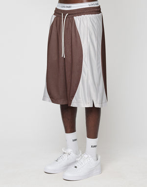 A person wearing LIVE FAST DIE YOUNG LFDY League Shorts in brown and white, white LIVE FAST socks, and logo-print white sneakers stands against a plain white background. The photo is cropped at the waist.