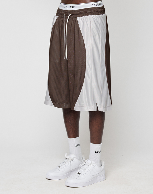 Wearing LFDY League Shorts by LIVE FAST DIE YOUNG—brown and white mesh with a subtle logo-print and "LIVE FAST" on the waistband—paired with white socks and sneakers, a person stands against a plain white background.
