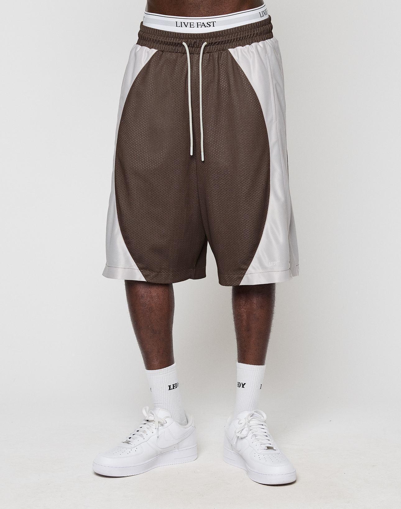 A person in LFDY League Shorts by LIVE FAST DIE YOUNG, white LIVE FAST waistband underwear, white socks, and white sneakers stands against a plain white background.
