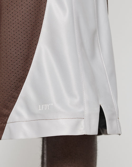 Close-up of the lower part of LFDY League Shorts by LIVE FAST DIE YOUNG in brown and white polyester, featuring mesh and smooth textures with a logo print near the hem.