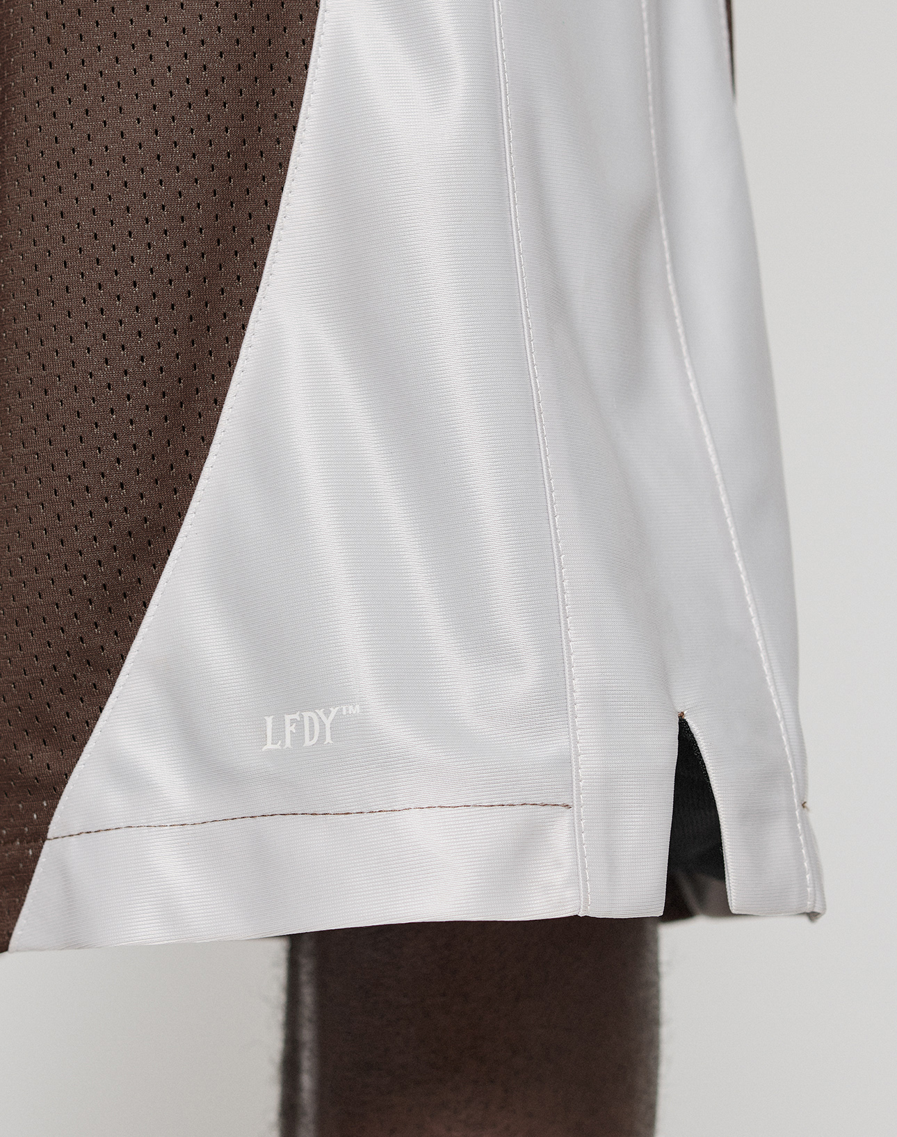 Close-up of a person wearing LIVE FAST DIE YOUNG’s LFDY League Shorts, featuring brown and white panels with a bold "LFDY" logo print. The shiny fabric and visible stitching create a standout, sporty look.