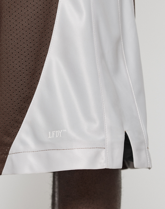 Close-up of a person wearing LIVE FAST DIE YOUNG’s LFDY League Shorts, featuring brown and white panels with a bold "LFDY" logo print. The shiny fabric and visible stitching create a standout, sporty look.