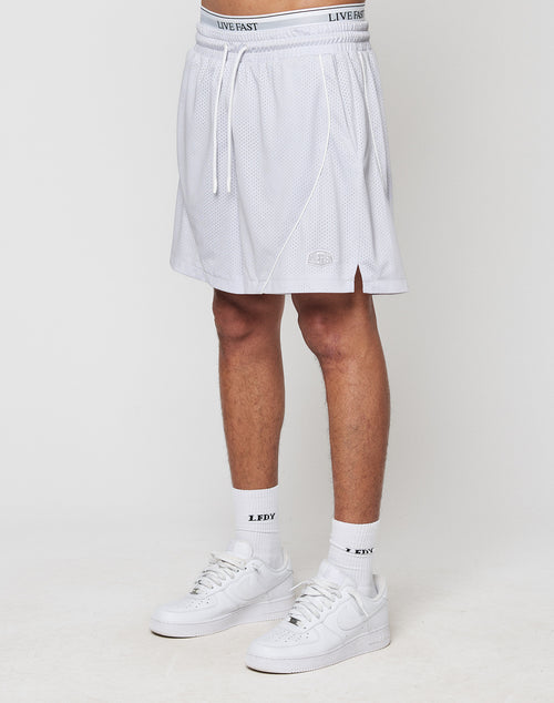 A person in white LIVE FAST DIE YOUNG LFDY Piping Mesh Shorts with a regular fit, elastic waistband, drawstring, and small logo near the hem, paired with white LFDTY socks and sneakers, stands against a plain light background.