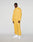 A man faces the camera against a plain gray background, wearing LIVE FAST DIE YOUNGs LFDY Trackpants—a loose-fit yellow polyester tracksuit with high collar, elastic waistband, white sneakers, and reflective print accents.