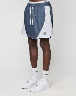 A person wears blue and white LFDY Piping Mesh Shorts by LIVE FAST DIE YOUNG with a LIVE FAST waistband, white socks with LED text, and white Nike sneakers, standing against a plain white background.