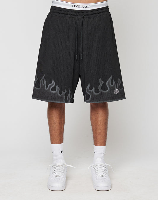 A person wears LIVE FAST DIE YOUNG Burning Mesh Shorts with gray flame print along the hem, LIVE FAST on the elastic waistband, paired with white socks and sneakers. Photo shows a plain background.