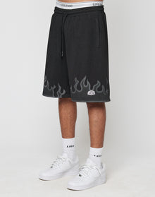 A person wears LIVE FAST DIE YOUNG Burning Mesh Shorts with a Flammenprint hem and elastic waistband, showing the white underwears band above. Paired with white socks and sneakers, theyre photographed against a plain background.
