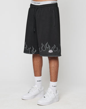 A person wears LIVE FAST DIE YOUNG Burning Mesh Shorts with a Flammenprint hem and elastic waistband, showing the white underwears band above. Paired with white socks and sneakers, theyre photographed against a plain background.