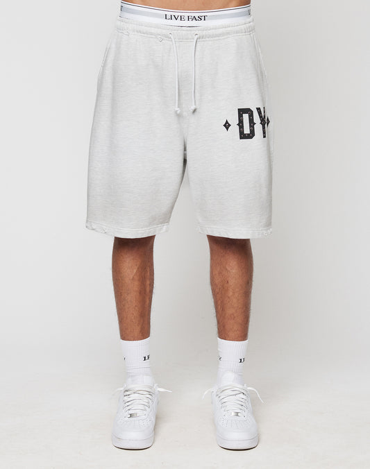Someone stands against a plain background wearing DY Rivet Shorts by LIVE FAST DIE YOUNG—light gray, oversize fit with DY on the left leg, a white waistband featuring LIVE FAST, paired with white socks and sneakers.