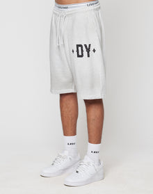 A person in LIVE FAST DIE YOUNG DY Rivet Shorts (light gray, 100% Baumwolle) with DY on the left leg, white LFDY socks, and white Nike sneakers stands against a plain white background.
