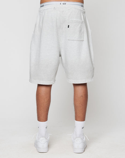 A person faces away, wearing LIVE FAST DIE YOUNGs DY Rivet Shorts in light gray with a back pocket and LEISURE-print waistband. Made from 100% Baumwolle, theyre paired with white socks and sneakers for comfort and style.
