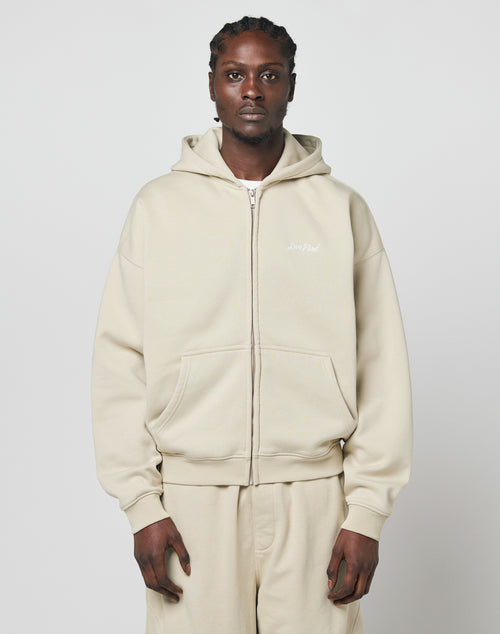 A person with braided hair wears a beige LIVE FAST DIE YOUNG Basic Script Hooded Zip and matching pants, standing against a plain light gray background.