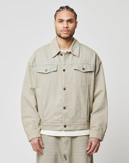 A man with braided hair and a trimmed beard wears the oversized fit Live Fast Denim Jacket by LIVE FAST DIE YOUNG, made from 100% Baumwolle in light beige, over a white shirt and matching pants against a plain light background.