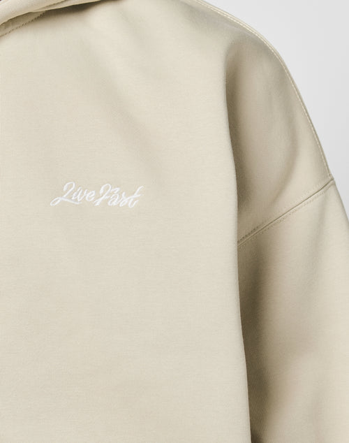 A close-up of the beige LIVE FAST DIE YOUNG Basic Script Hooded Zip, featuring the 2LivePart Logo-Stick embroidered in white on the chest.