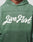 A person wearing an oversize LFDY Script Hooded by LIVE FAST DIE YOUNG in green, featuring “Live Fast” in bold white script on the chest and subtle Sprayeffekt accents.