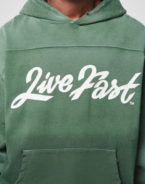 A person wearing an oversize LFDY Script Hooded by LIVE FAST DIE YOUNG in green, featuring “Live Fast” in bold white script on the chest and subtle Sprayeffekt accents.