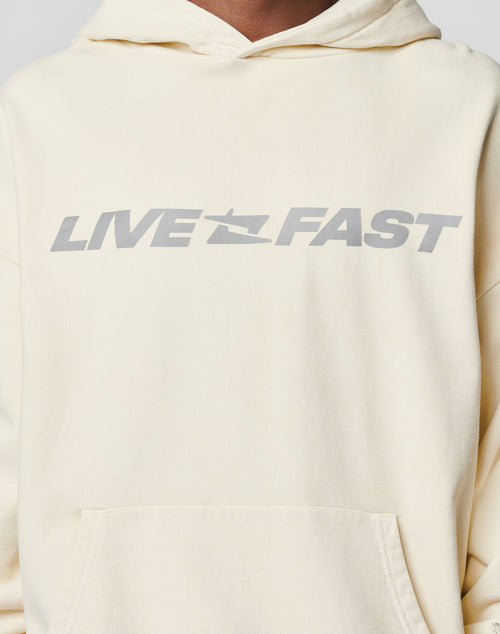 A person wears a light beige LIVE FAST DIE YOUNG LFDY Window Hooded, featuring bold gray LIVE FAST text and a small jet graphic in the center. The reflektierender Druck adds standout style.
