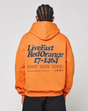 A person with braided hair wears the Basic Orange Hooded by LIVE FAST DIE YOUNG, made of polyester and cotton, featuring a bold black and white Live Fast Red Orange 17-1464 front and back print plus extra small text and symbols.
