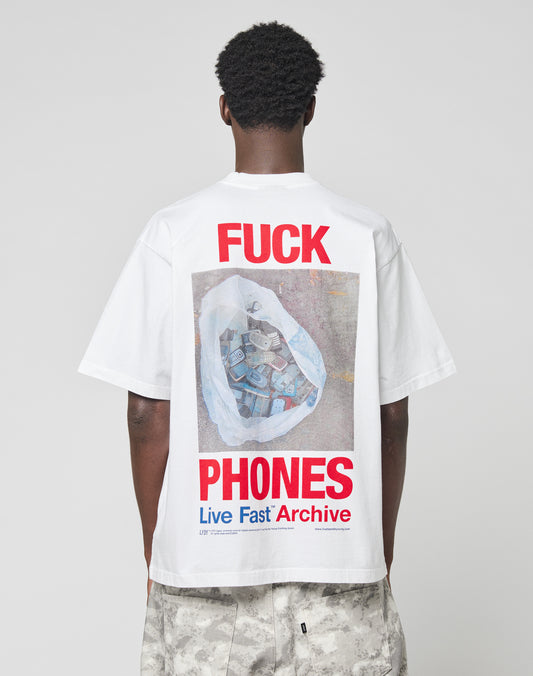 A person faces away, showing the back of the LFDY F*ck Phones Tee by LIVE FAST DIE YOUNG: an oversize cotton tee with bold red “FUCK PHONES” text and a photo of a trash bag full of phones, plus blue “Live Fast Archive” text below.