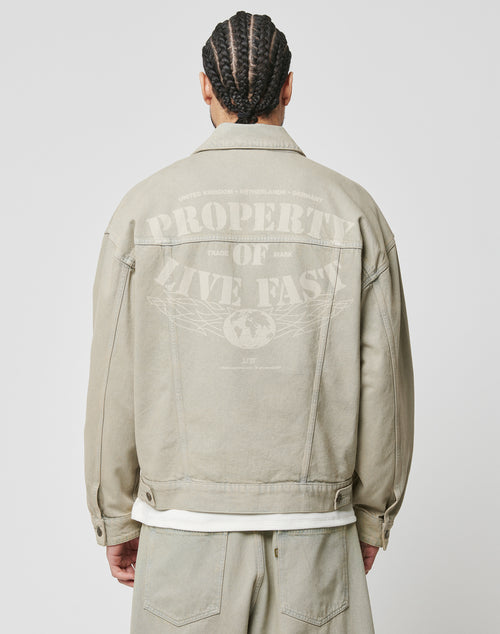 A person with braided hair is seen from behind wearing the Live Fast Denim Jacket by LIVE FAST DIE YOUNG. The 100% Baumwolle jacket has an oversized fit and PROPERTY OF LIVE FAST with a globe and country names printed on the back.