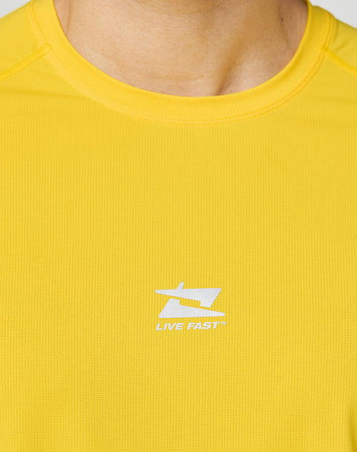 Close-up of a person wearing the LIVE FAST DIE YOUNG Live Fast Performance Longsleeve in bright yellow, featuring a white LIVE FAST logo and reflective front print on the chest. The slim fit highlights their build; neck and chin are visible.