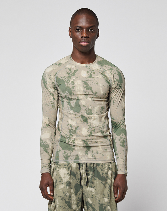 A person wears the LIVE FAST DIE YOUNG LFDY Performance Slim Longsleeve and matching shorts in green and beige camouflage with leichtes Obermaterial, standing against a plain white background.