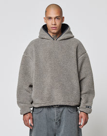 A person with a shaved head wears the LIVE FAST DIE YOUNG LFDY Teddy Hooded in gray, featuring practical Eingrifftaschen, and loose-fitting gray jeans, standing against a plain white background.