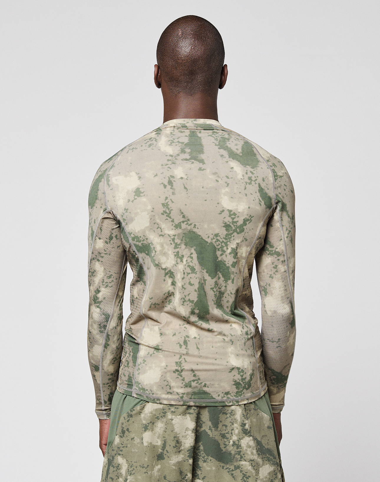 A person with a shaved head, seen from behind, wears the LFDY Performance Slim Longsleeve by LIVE FAST DIE YOUNG and green-beige camo shorts against a plain white background.