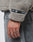 A close-up of a hand with “TIME” tattooed on the fingers, wearing grey jeans and an oversized beige LIVE FAST DIE YOUNG LFDY Teddy Hooded fleece with a black LFDY web label on the sleeve.