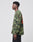 A person stands in profile against a plain background, wearing the LIVE FAST DIE YOUNG Copyright Waffle Longsleeve in green camo with an orange backprint, made from 100% cotton and featuring an oversize fit, paired with black pants.