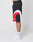 A person stands in profile against a white background wearing LIVE FAST DIE YOUNG Basic Trackshorts in black, red, and white logo-print polyester, paired with white LEDY socks and white sneakers.