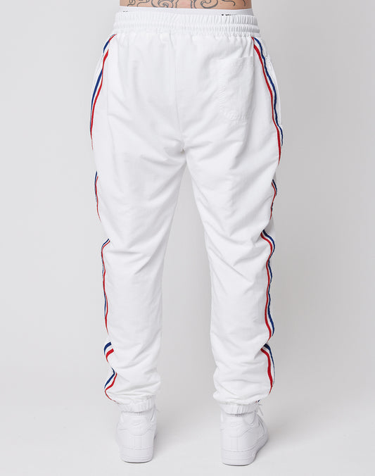 Person seen from the back wearing LFDY x Trigema Trackpants by LIVE FAST DIE YOUNG, featuring red and blue side stripes, regular fit, white sneakers, and a tattoo visible on the lower abdomen.