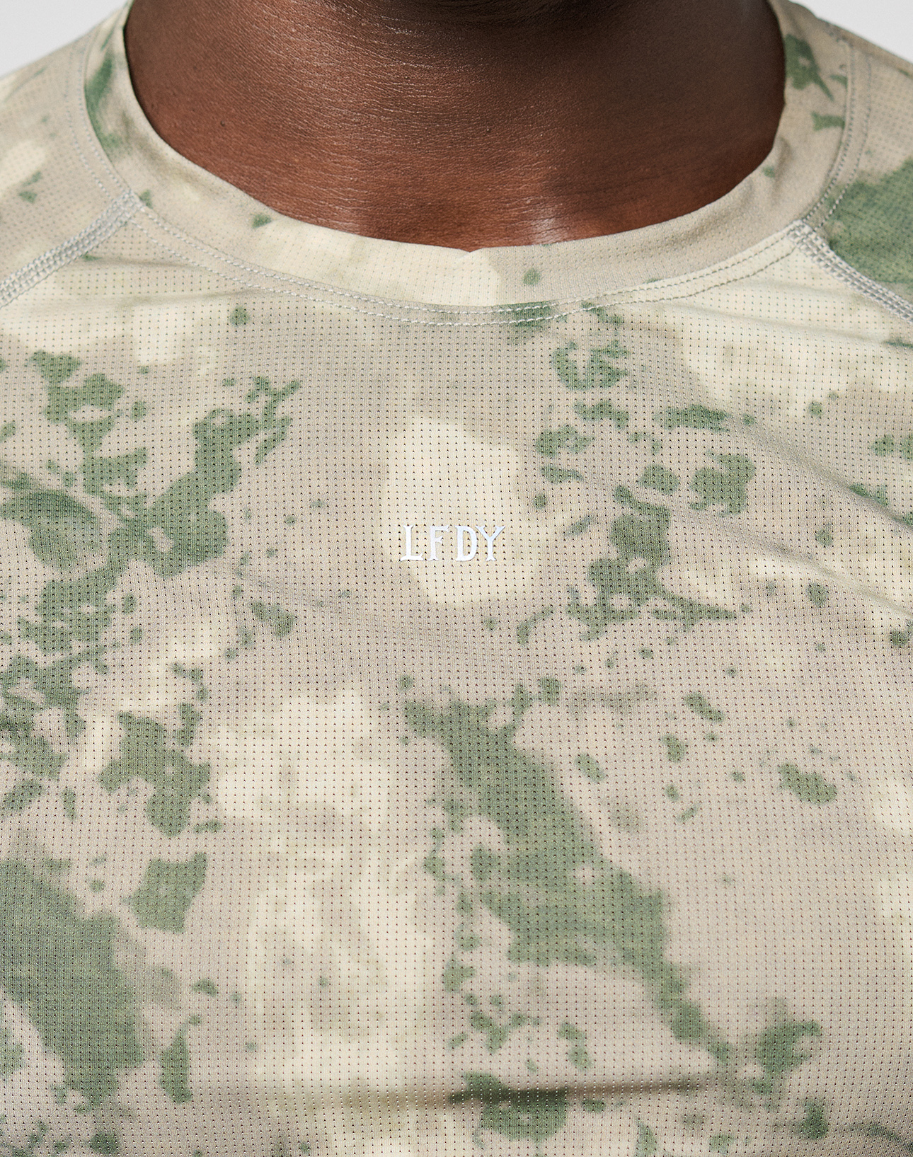 Close-up of a person wearing the LIVE FAST DIE YOUNG LFDY Performance Slim Longsleeve in light beige and green camouflage, featuring a reflective WILDR logo on the chest. Only the lower face and neck are shown.