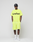 A person stands against a plain background, wearing a neon yellow Regular Fit LIVE FAST DIE YOUNG t-shirt with logo print, Basic Shorts with elastic waistband, white socks, white sneakers, and a black baseball cap. Their hands are in their pockets.