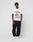 A man stands against a plain white background wearing a LIVE FAST DIE YOUNG Abus Magomedov Tee with TEAM ABUS MAGOMEDOV front and backprint, black sweatpants, and white sneakers. He has a neutral expression and his hands in his pockets.